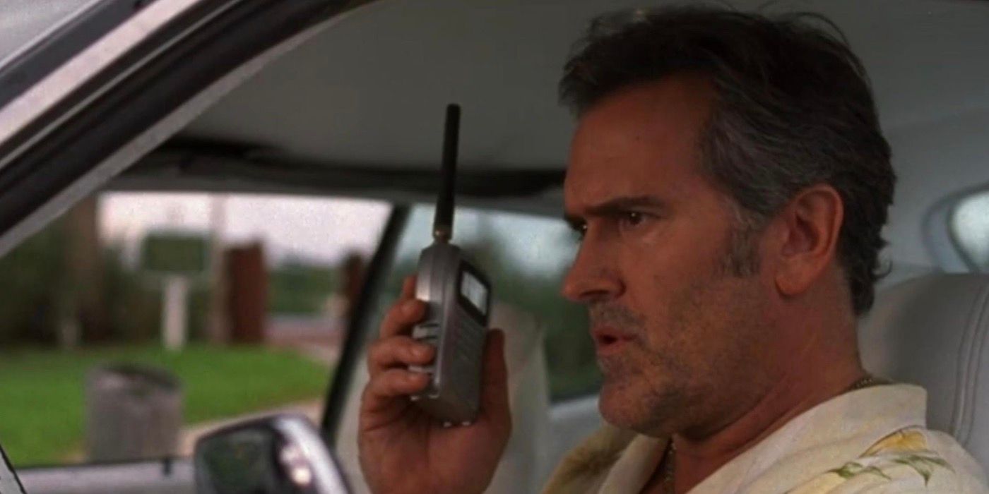 Sam Axe is sitting in a car while holding up a walkie-talkie. 