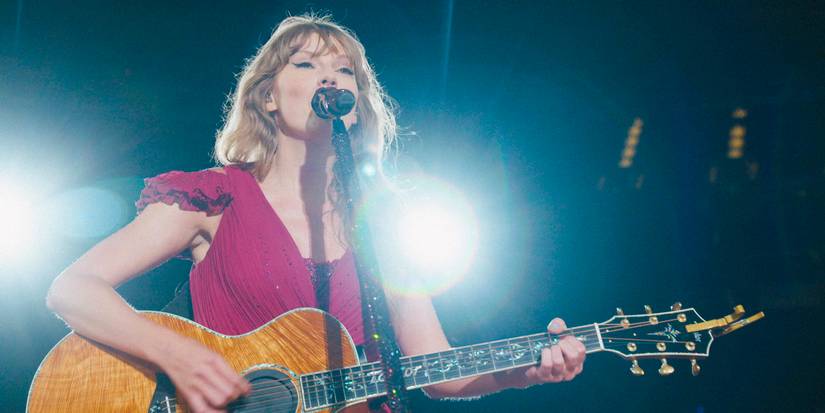 Close-up shot of Taylor Swift standing in front of the microphone, playing the guitar, and wearing a red dress from the Eras Tour