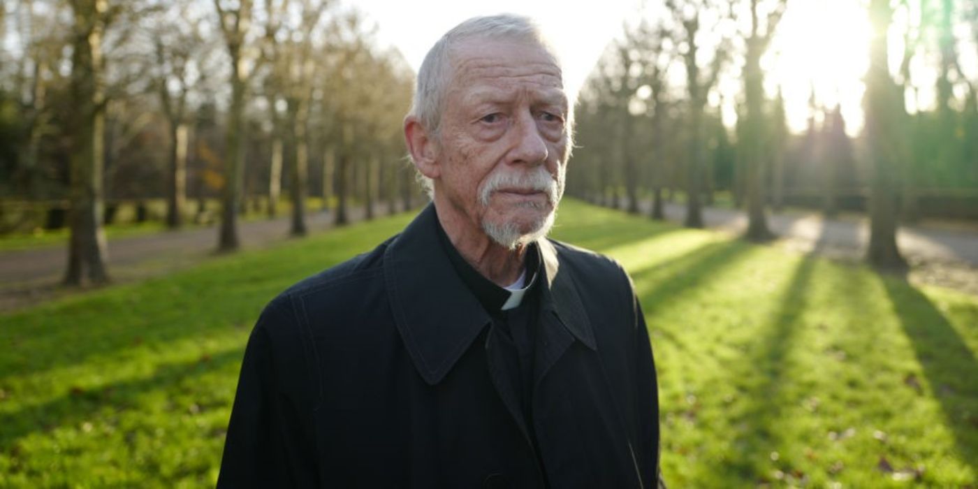 The Priest (John Hurt) standing in a field in Jackie.