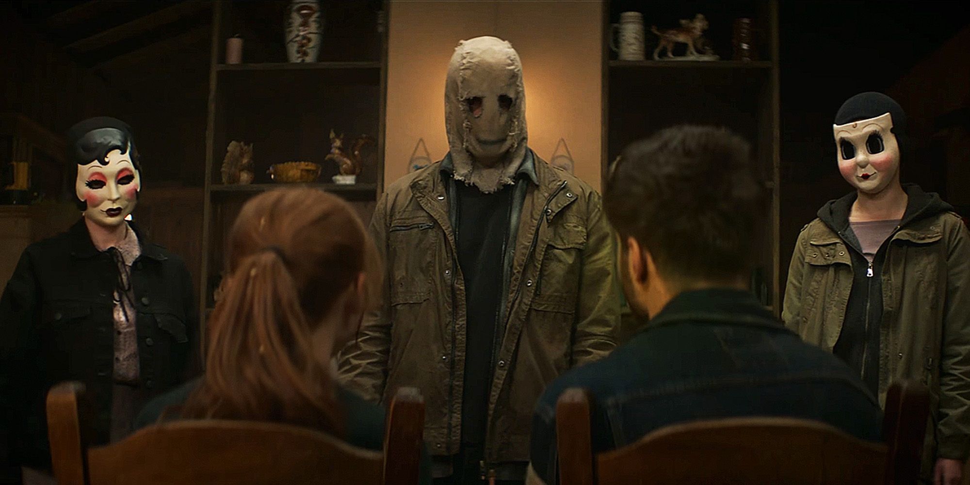 three masked people standing in front of a couple sitting down in The Strangers Chapter 1