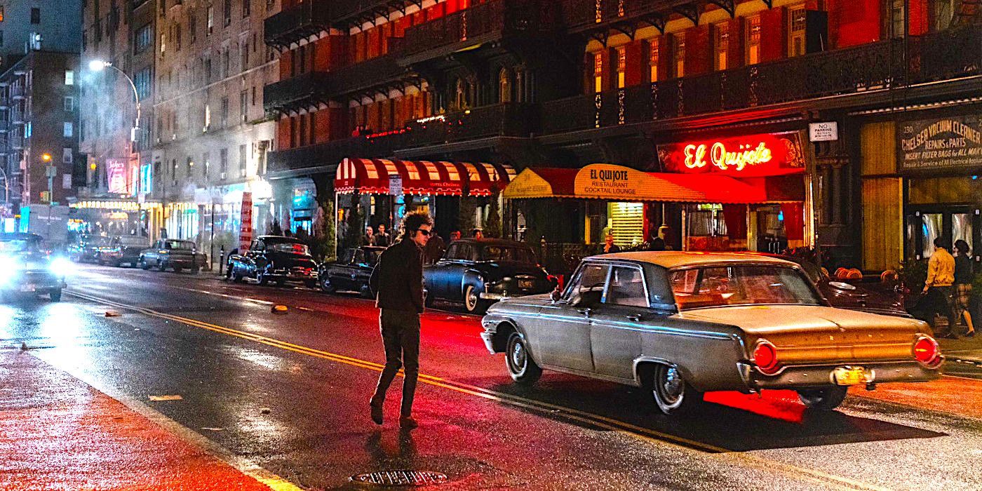 Timothee Chalamet as Bob Dylan crosses a rainy New York street with neon signs reflected on the pavement in a scene from A Complete Unknown