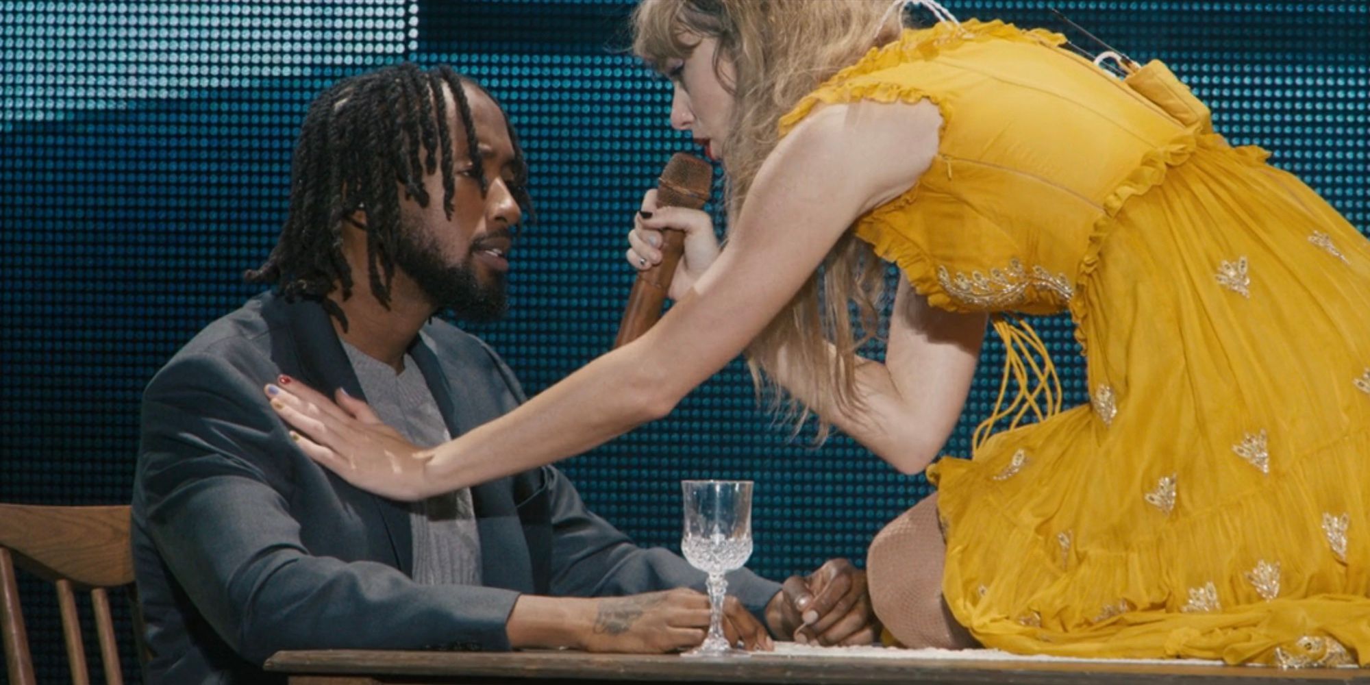 Taylor Swift kneels on top of a table and touches backup dancer Raphael Thomas' chest while performing "tolerate it" in The Eras Tour movie.
