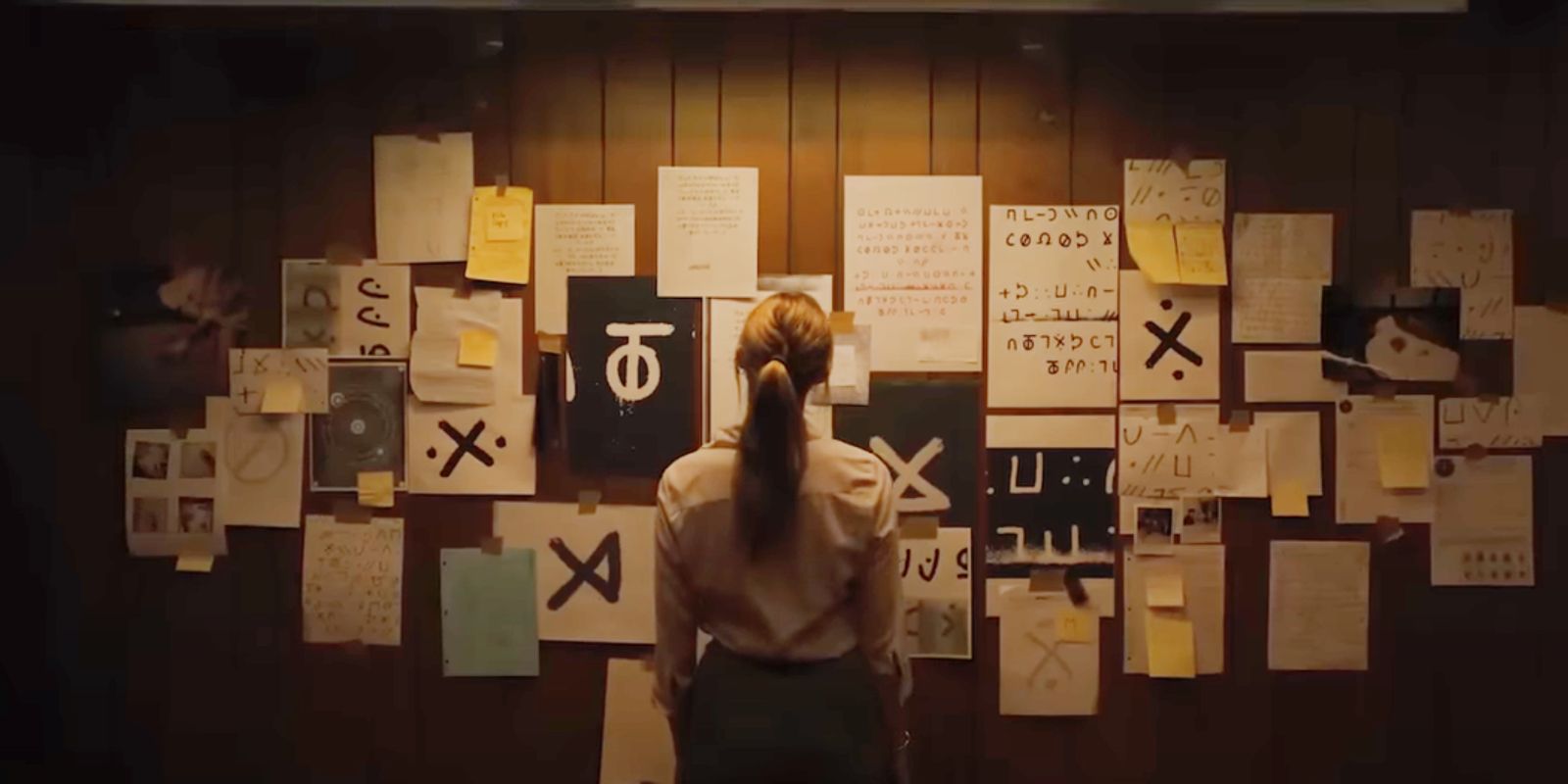 Kobieta patrząca na papiery z dziwnymi symbolami rozrzucone po ścianie w Longlegs