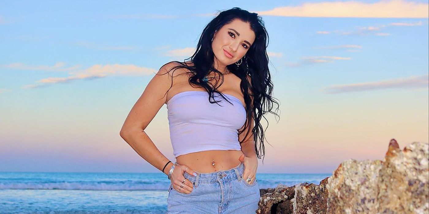 Xandi Olivier from Below Deck posing on a beach in a tube top and jeans