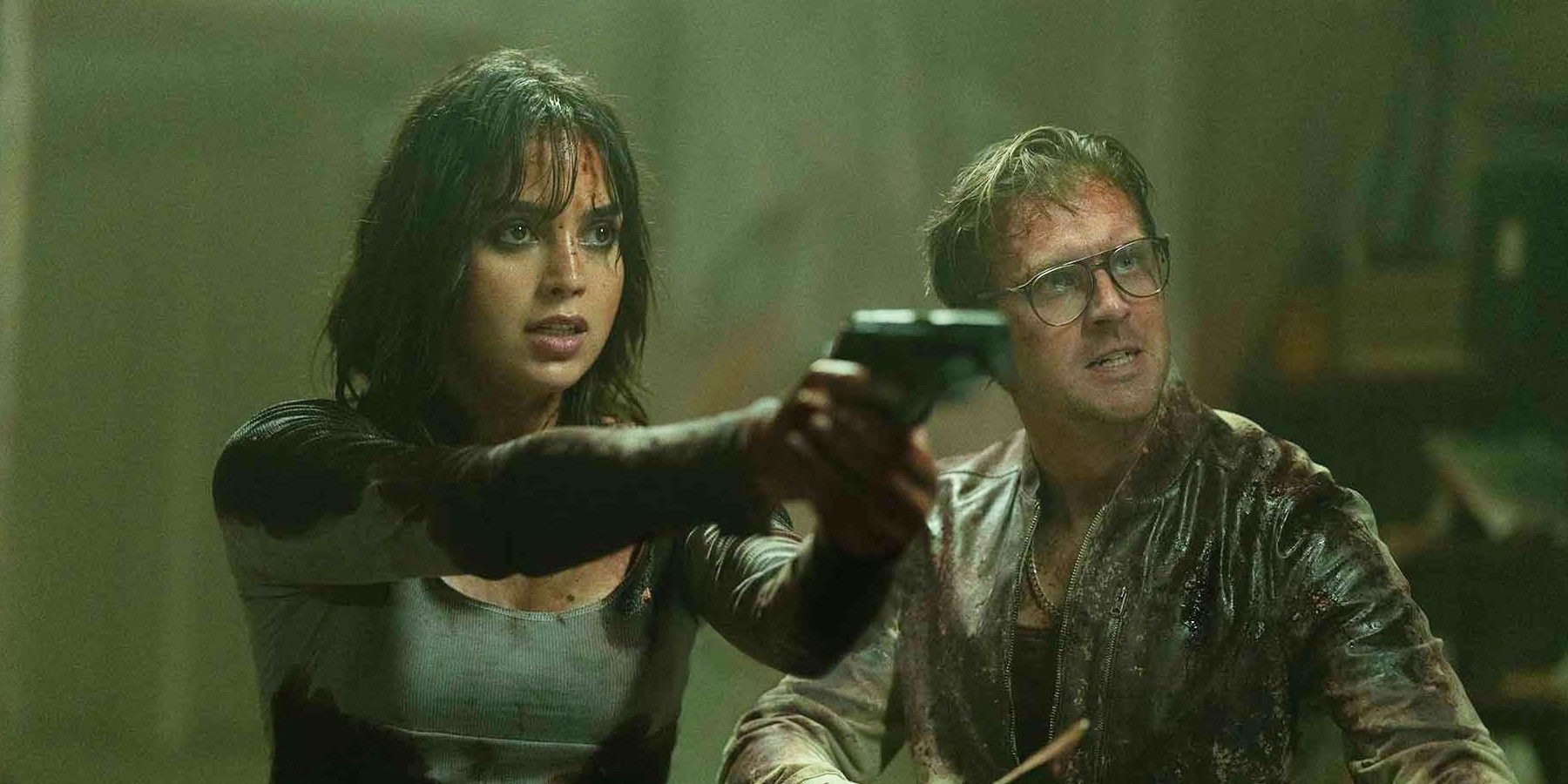 a bloody Melissa Barrera pointing a gun next to a bloody Dan Stevens in a fighting stance in Abigail