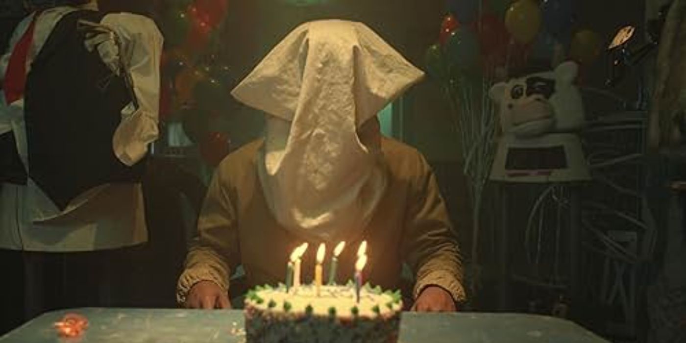 Um personagem com um saco na cabeça sentado em frente a um bolo de aniversário em Them: The Scare