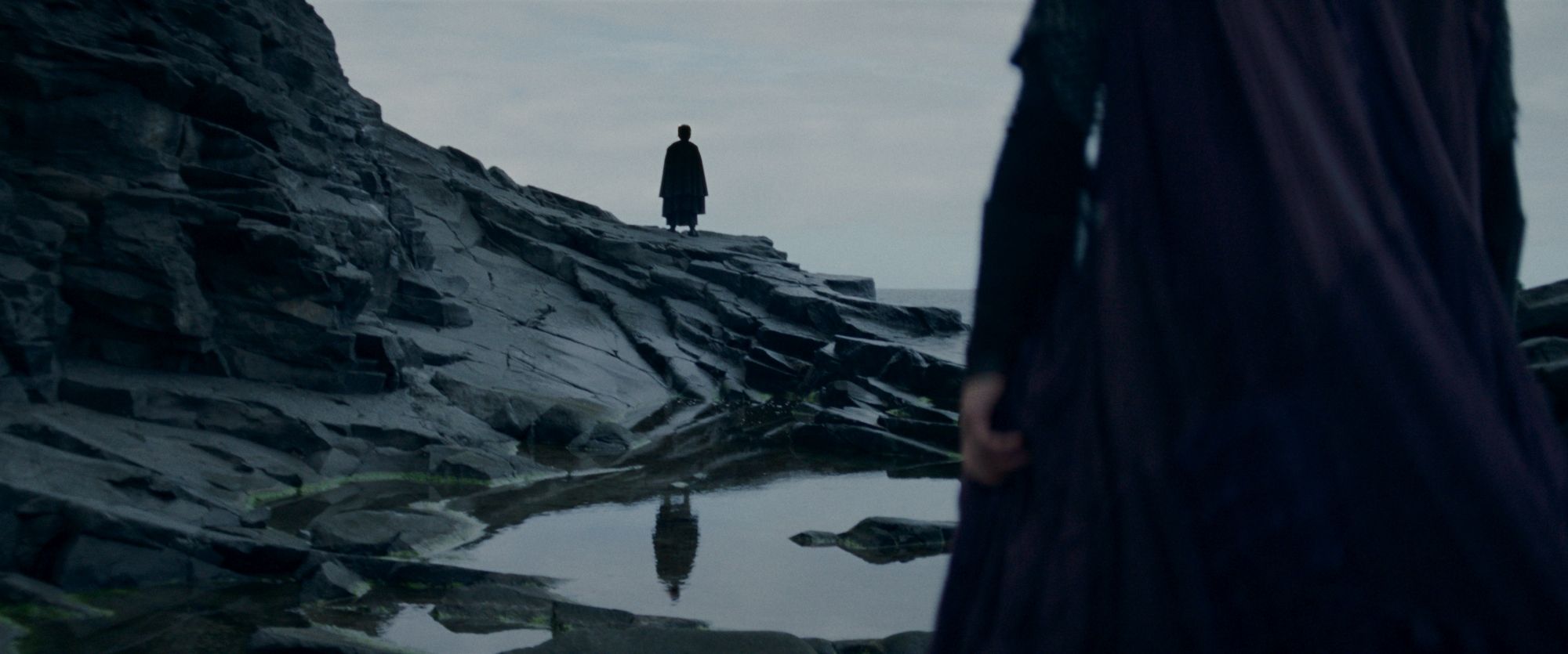 Mae (Amandla Stenberg) é vista por trás olhando para uma figura misteriosa parada em um afloramento rochoso em Star Wars: The Acolyte