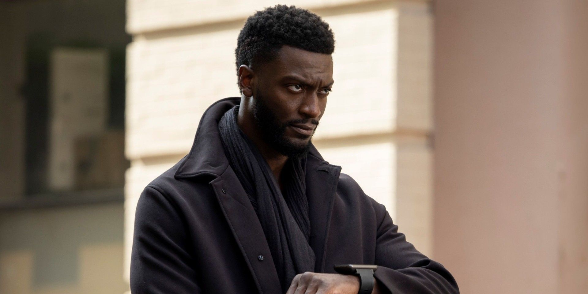 Aldis Hodge as Hardison standing in the middle of a street with his hand raised as if to look at his watch, but is actually looking forward in Leverage Redemption