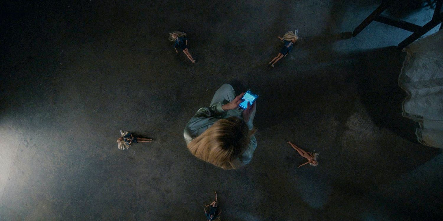 Foto aérea de Anna Victoria Alcott cercada por 5 bonecas Barbie enquanto olha para seu celular em American Horror Story: Delicate temporada 12, episódio 6