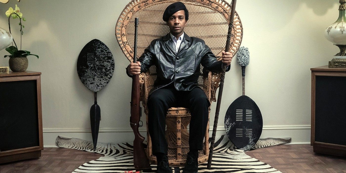André Holland as Huey P. Newton holding a rifle and a staff while sitting in a chair in the trailer for The Big Cigar