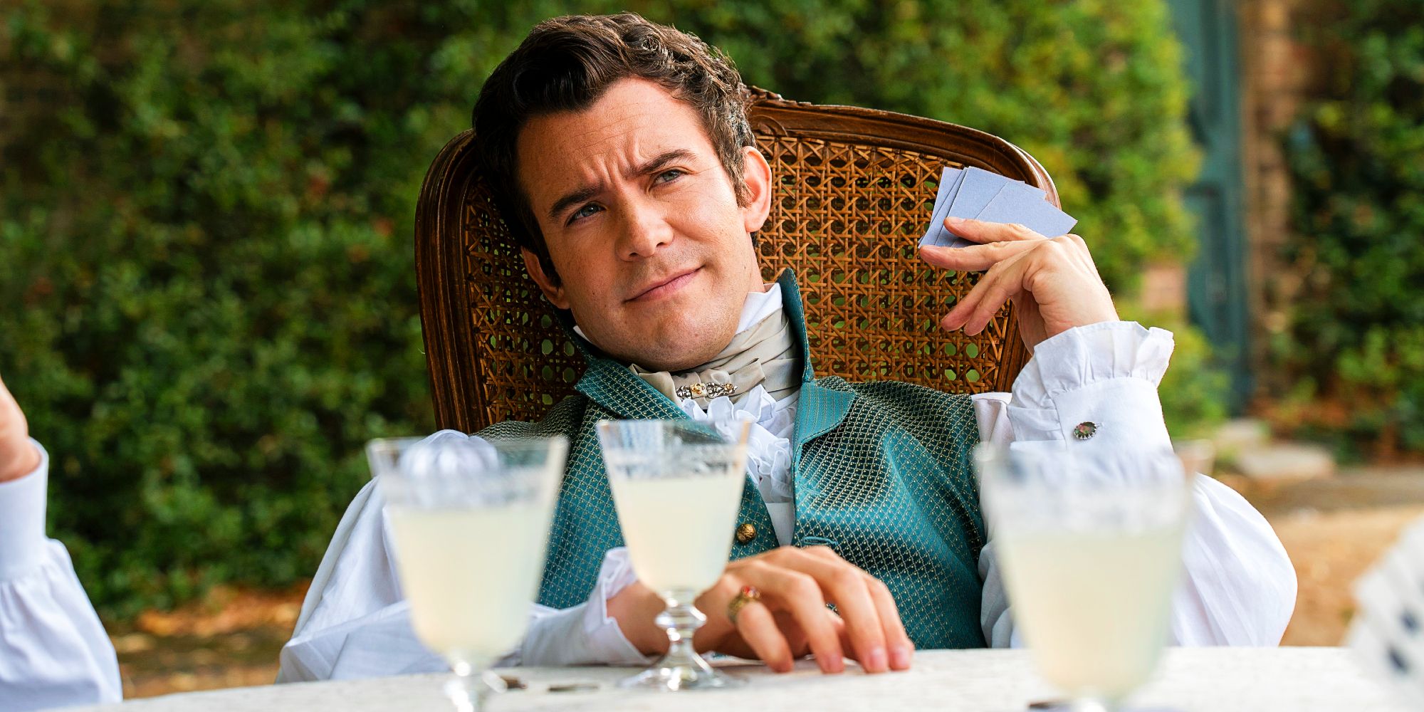 Luke Thompson as Benedict Bridgerton playing cards with drinks in front of him in Bridgerton season 3 episode 2