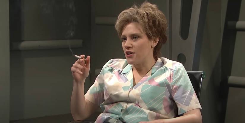 Kate McKinnon is sitting down with a cigarette in her hand.