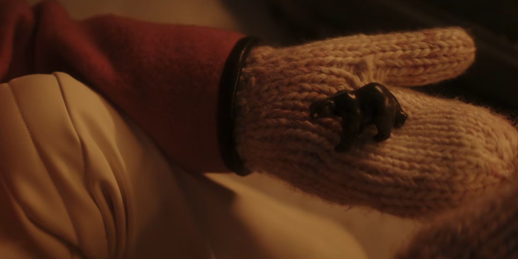 Uma mão enluvada segura um amuleto de urso em Dead Boys Detectives