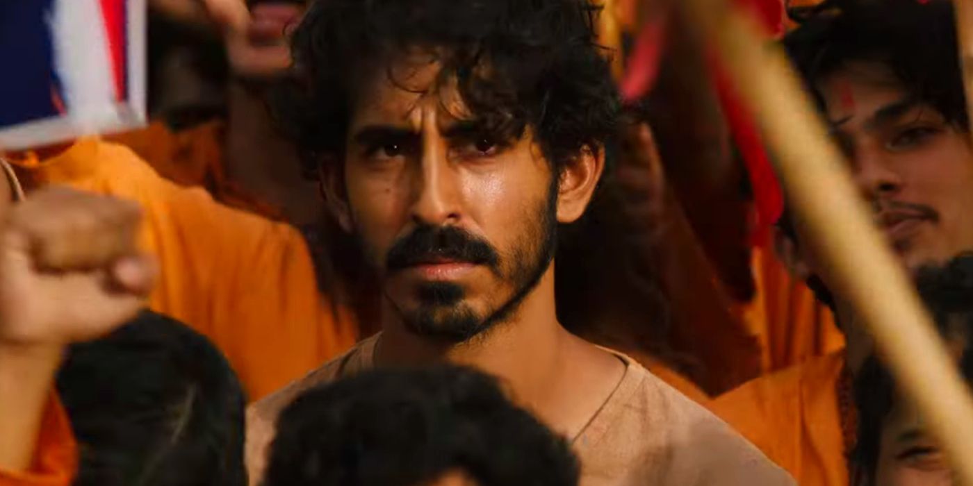 Dev Patel as Kid in a Crowd in Monkey Man. He looks confused. He is wearing a tan shirt and those around him are wearing orange.