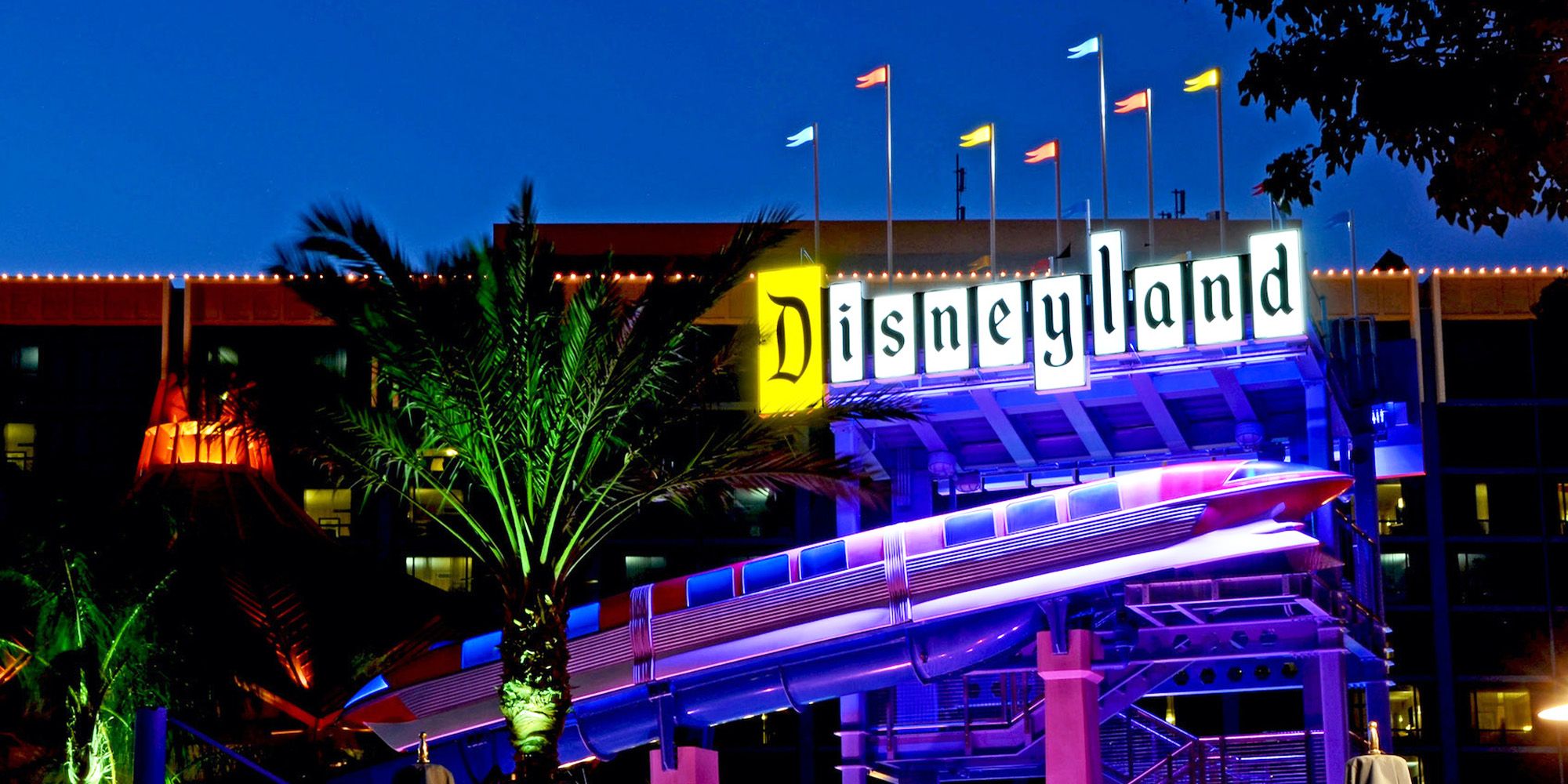 Uma placa da Disneylândia com bandeiras e uma estátua de um monotrilho abaixo dela