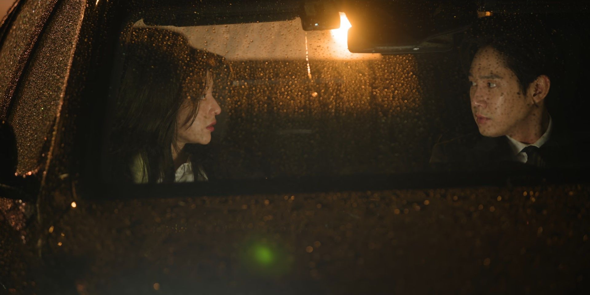 Haein and Eunsung look at one another whilst sat in a rain covered car in Queen of Tears