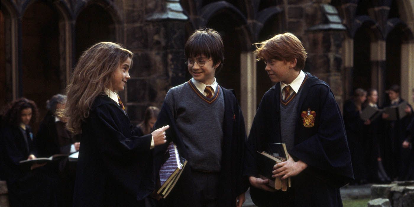 Hermione, Harry e Ron segurando livros e conversando no pátio de Hogwarts