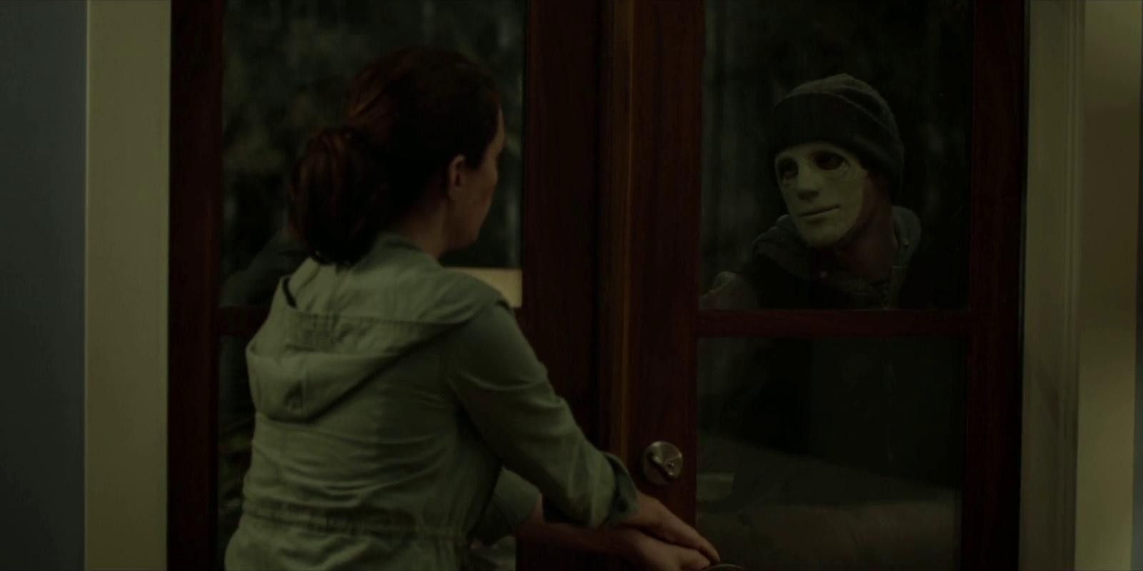 A masked man looks through a glass door in Hush