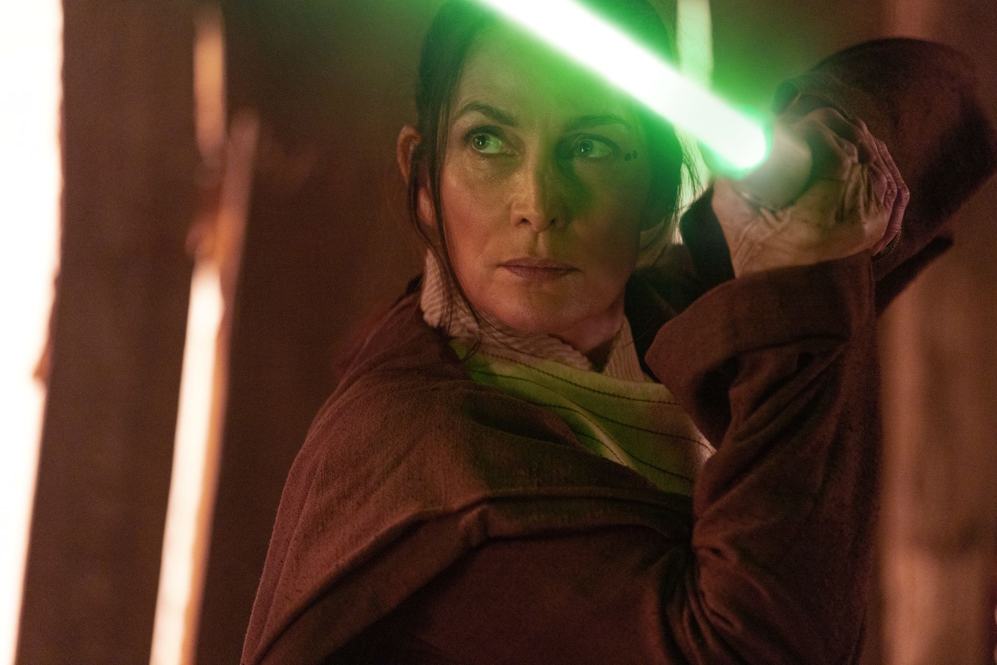 Close de Carrie-Anne Moss como Mestre Jedi Indara empunhando um sabre de luz verde em Star Wars: The Acolyte