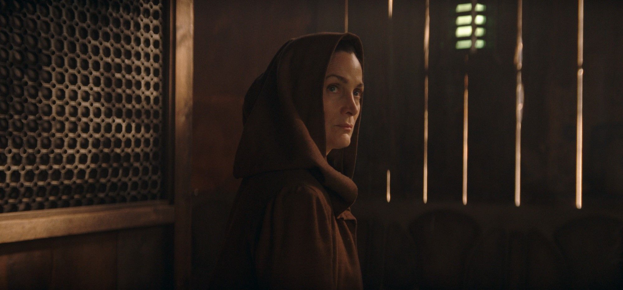 A Mestre Jedi Indara (Carrie-Anne Moss) está sentada em um canto com o capuz puxado sobre a cabeça em Star Wars: The Acolyte