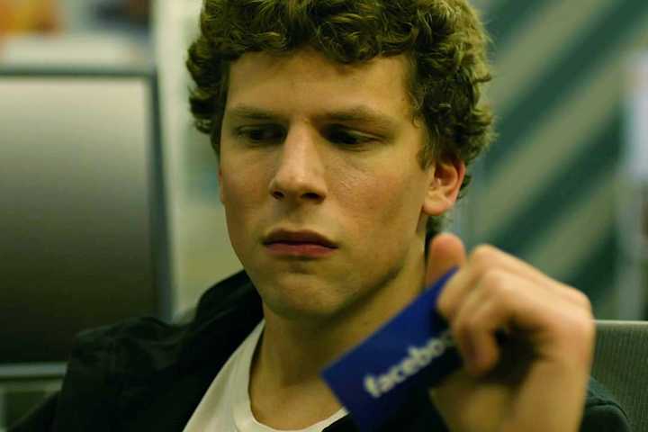 Jesse Eisenberg as Mark Zuckerberg looking sad while holding onto a Facebook card in The Social Network