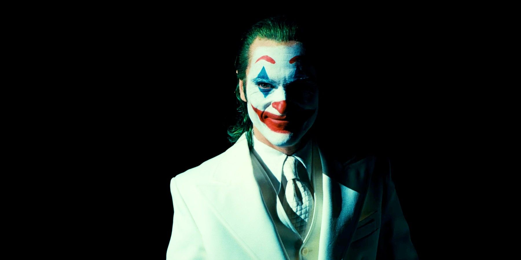 Joaquin Phoenix como Arthur Fleck em maquiagem Joker e terno branco em Joker Folie A Deux