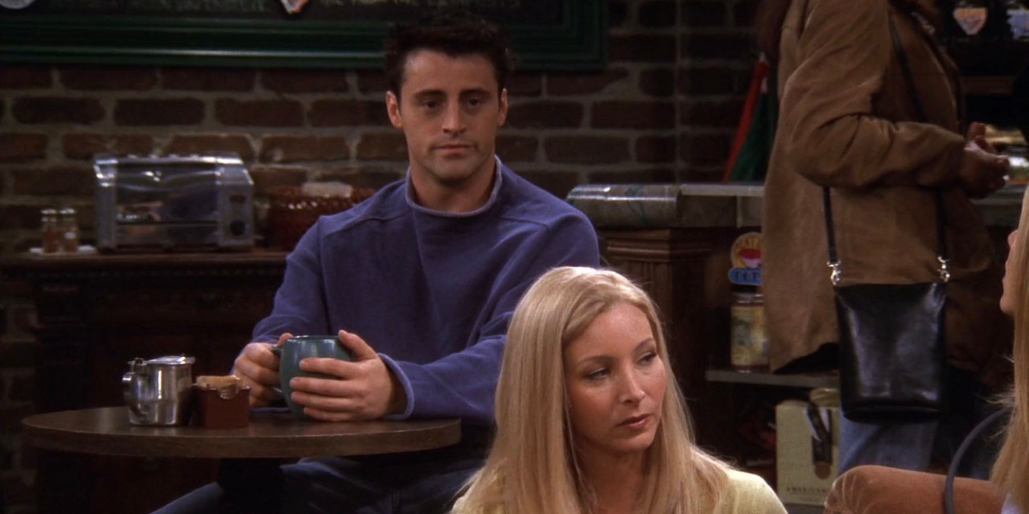 Phoebe (Lisa Kudrow) sits in front of Joey (Matt LeBlanc) while he clutches a coffee mug at Central Perk in Friends season 6, episode 8, 