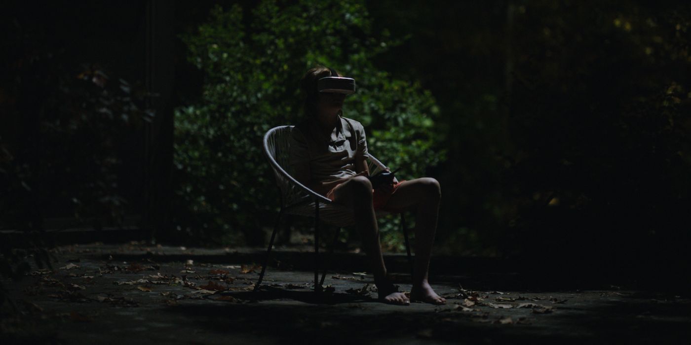 John (Charlie Shotwell) sitting with a VR mask at night in John and the Hole.