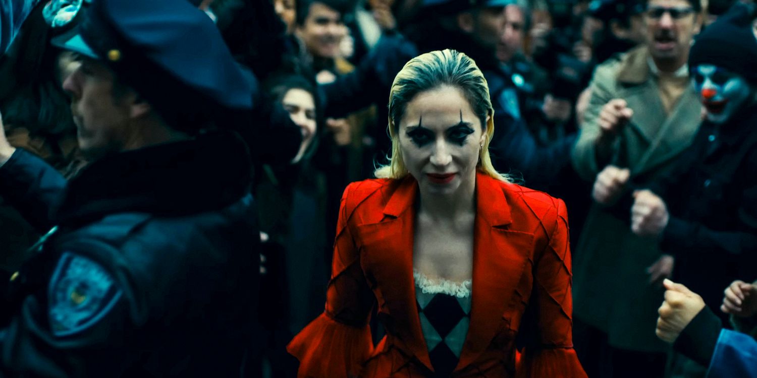 Harley Quinn (Lady Gaga) with jester-style makeup walks among a crowd of people and police officers in Joker: Folie à Deux