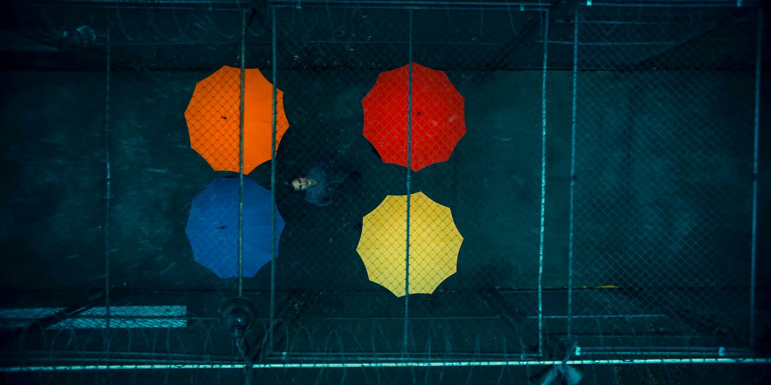 Aerial shot of Arthur Fleck (Joaquin Phoenix) looking up at the sky, escorted by four colorful umbrellas in Joker: Folie à Deux