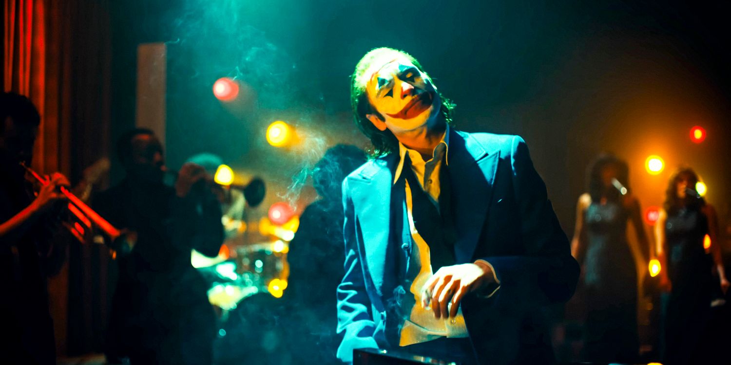 Arthur Fleck como o Coringa (Joaquin Phoenix) fuma um cigarro enquanto curte uma apresentação musical atrás dele em Joker: Folie à Deux
