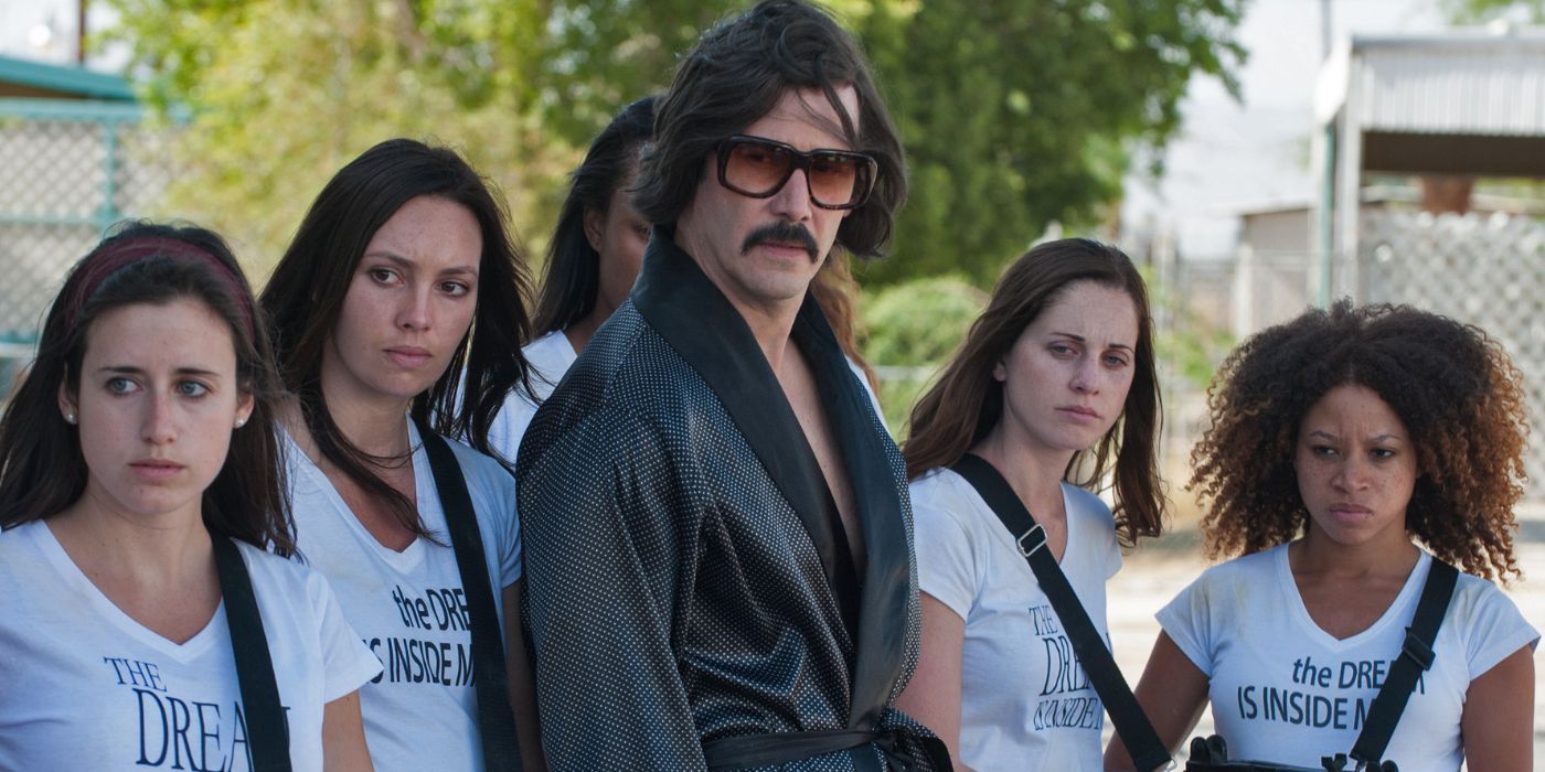 Keanu Reeves como The Dream está cercado por mulheres armadas em The Bad Batch.