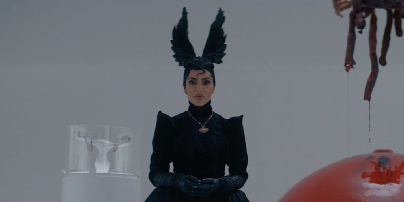 Siobhan de Kim Kardashian em pé em uma sala branca cercada por objetos bizarros no episódio 9 da 12ª temporada de American Horror Story