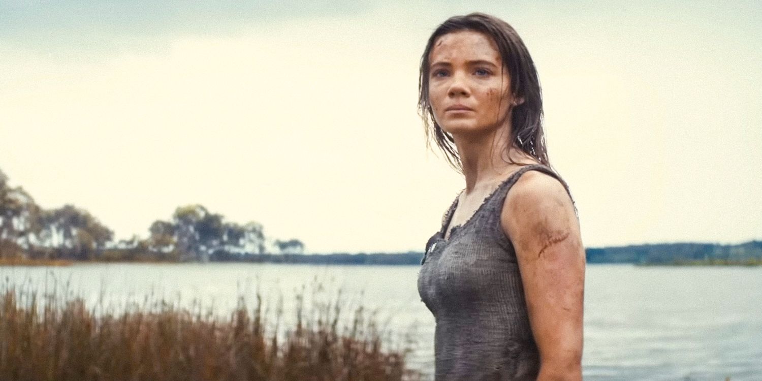 Mae (Freya Allan) with a dirty face and arms, with a lake behind her in Kingdom of the Planet of the Apes