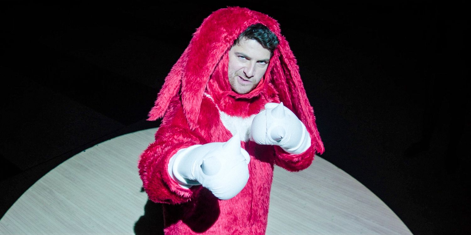 Wade Whipple wearing a Knuckles mascot suit illuminated by spotlight in Knuckles season 1