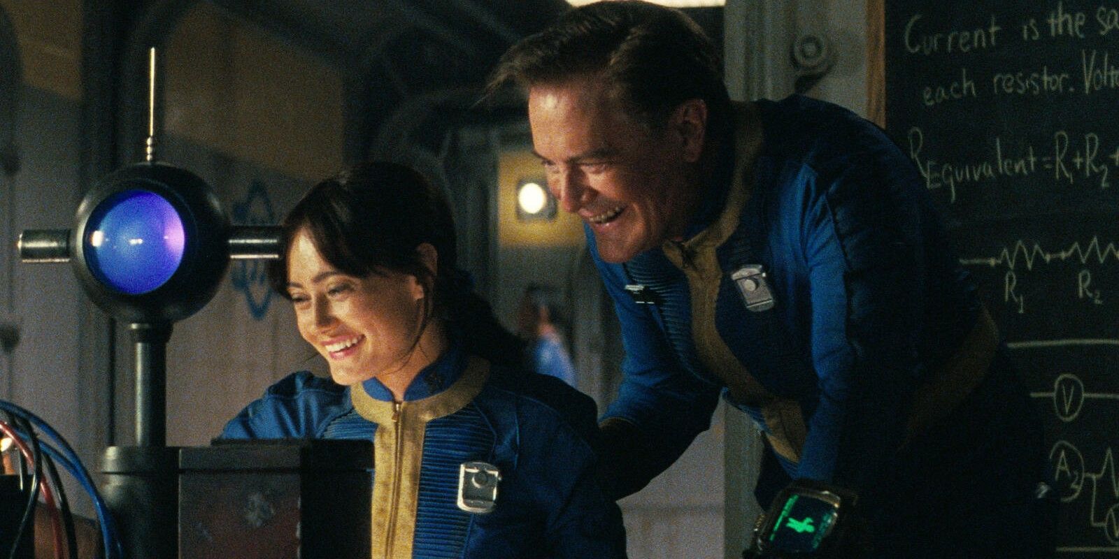 Lucy and Hank grinning down at something together, with Hank standing behind Lucy, in Fallout season 1