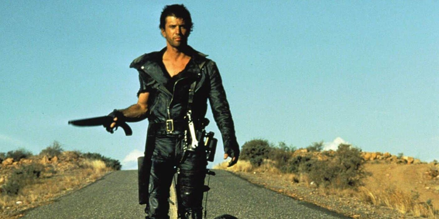 Mel Gibson as Max walking through a desert with a gun in Mad Max 2 The Road Warrior