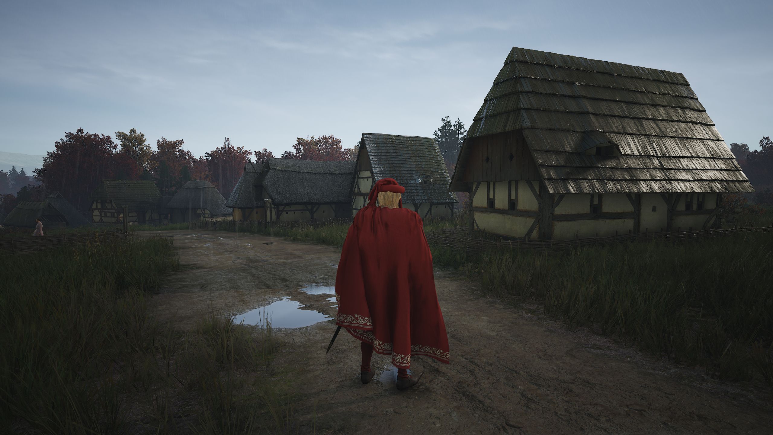 Jogador de Manor Lords em vestes vermelhas andando pela estrada de terra após os níveis 2 e 1 dos lotes de Burgage