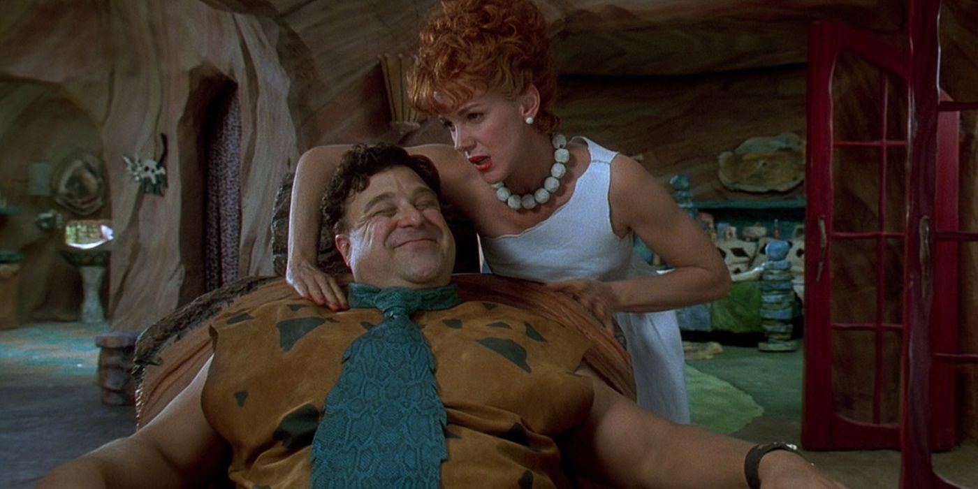 Fred (John Goodman) sorrindo enquanto Wilma (Elizabeth Perkins) lhe faz uma massagem nos ombros em Os Flintstones