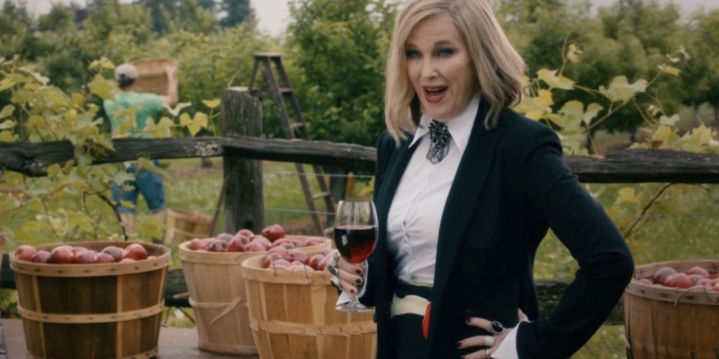 Moira (Catherine O'Hara) grins while holding a glass of wine in a vineyard in Schitt's Creek