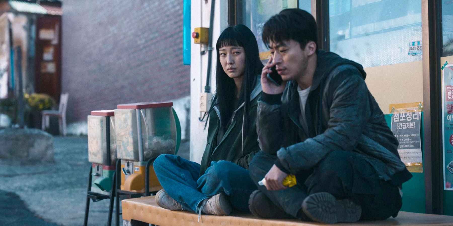 Jeong Su-in and Seol Kang-woo sitting on a bench while he talks on the phone in Parasyte: The Grey season 1 