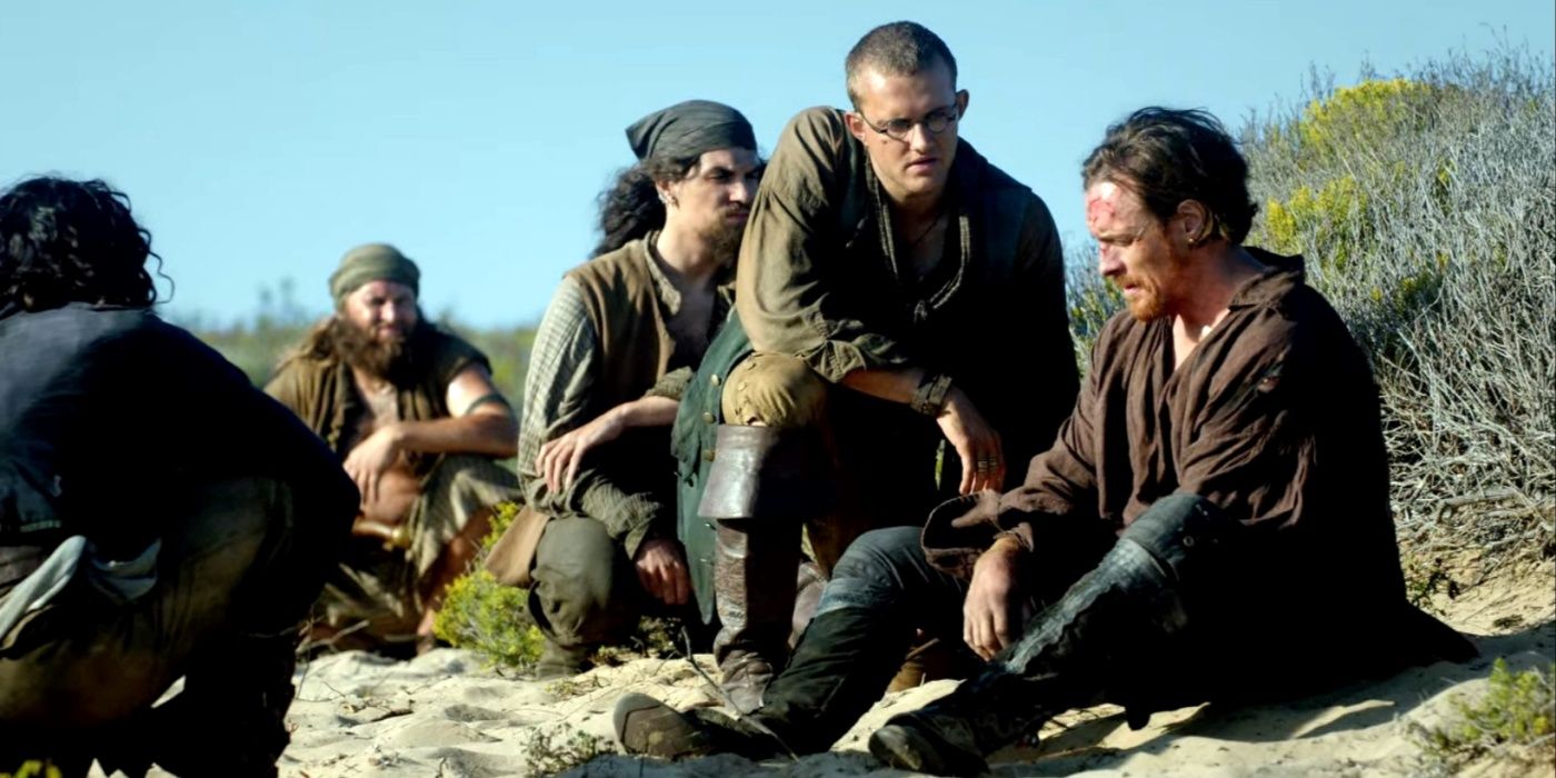 Dufresne (Roland Reed), Long John Silver (Luke Arnold), and Flint (Toby Stephens) sitting on the beach in Black Sails season 2