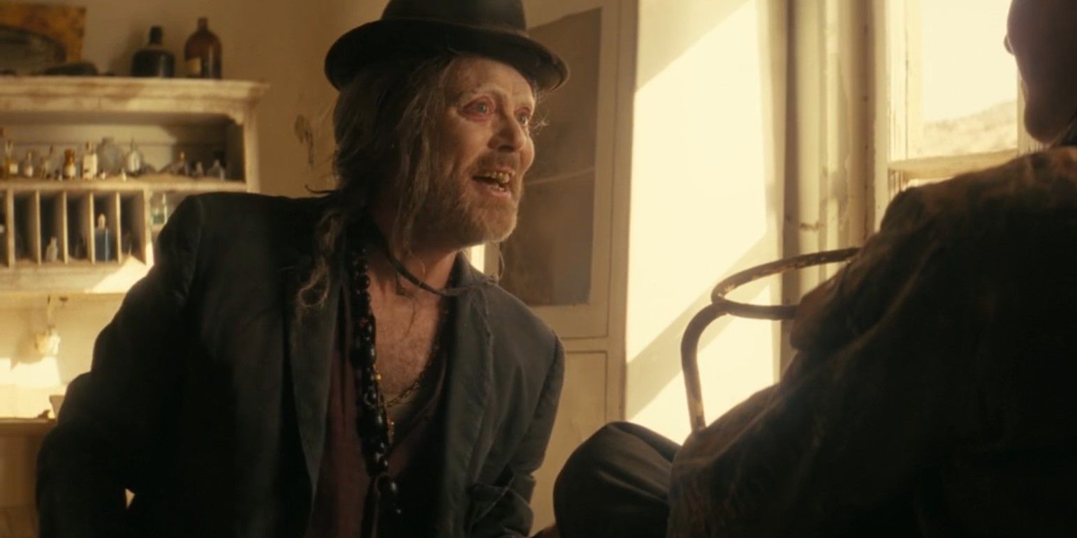 Jon Daly como o vendedor de óleo de cobra em Fallout sorrindo enquanto fala com Thaddeus