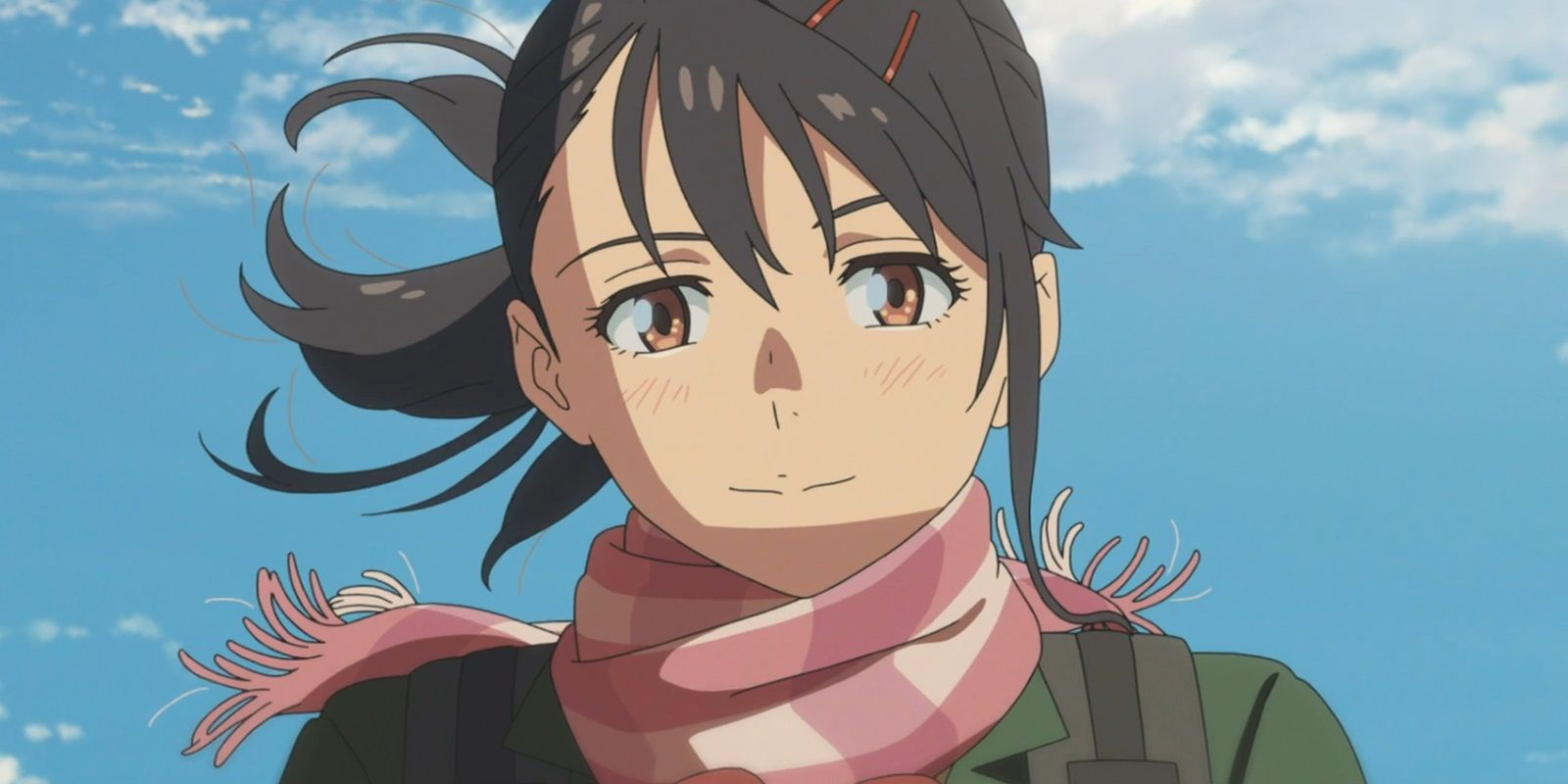 Suzume in the final scene of the film, smiling warmly while her hair and a scarf blow in the wind during a sunny day.