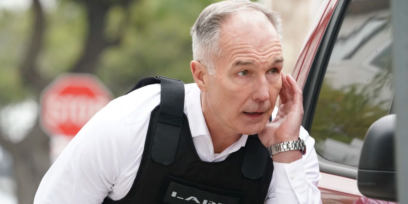 Commander Hicks crouches behind a car while talking into his earpiece in SWAT