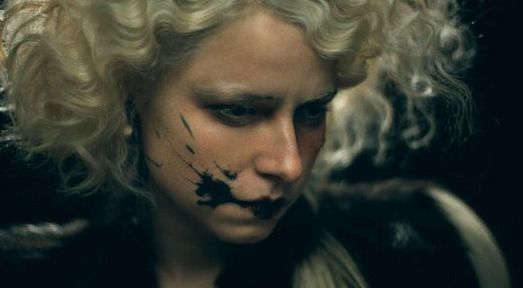 Jessie Buckley wears a blonde wig and has black paint splattered across her cheek in an image from The Bride