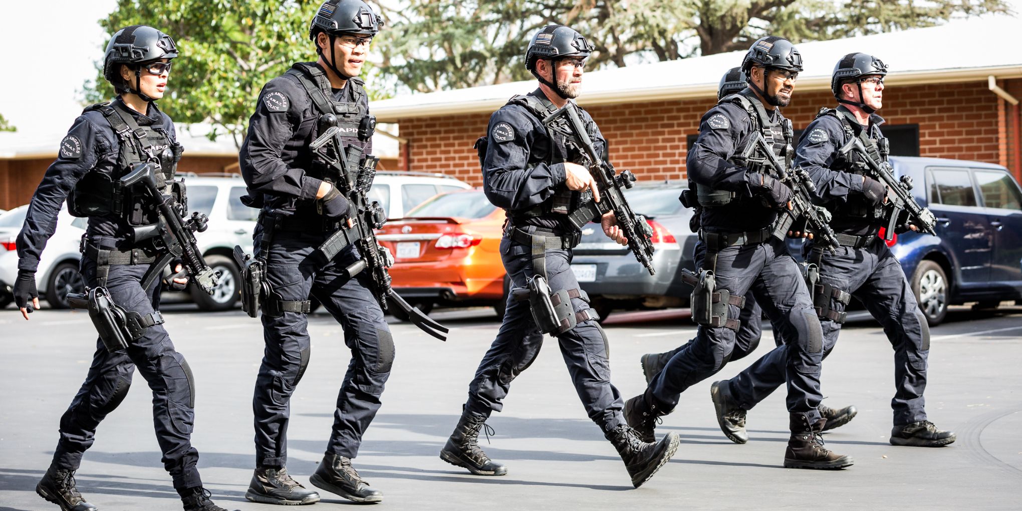Os integrantes da equipe principal uniformizados e caminhando por um estacionamento no episódio School da SWAT