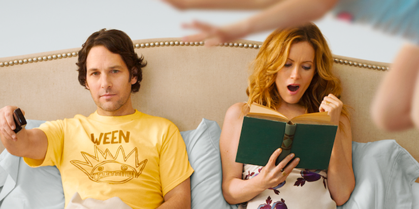 Pete (Paul Rudd) and Debbie (Leslie Mann) sitting in bed watching TV and reading a book in This Is 40.