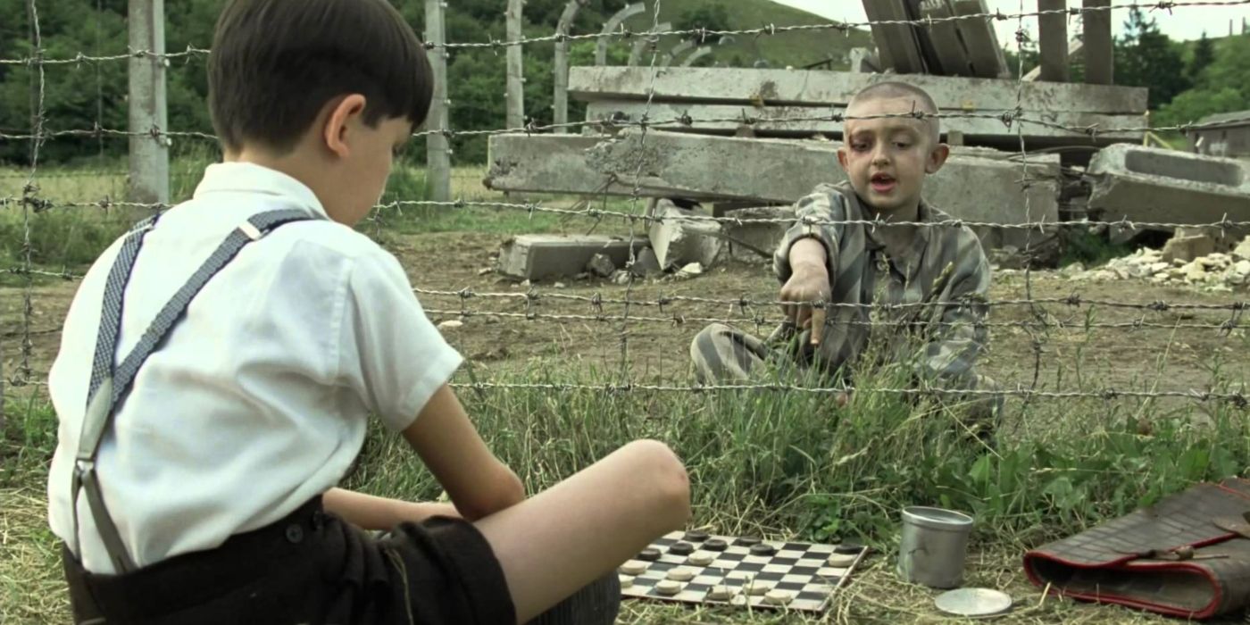 Dois meninos jogam damas em lados opostos de uma cerca em O Menino do Pijama Listrado