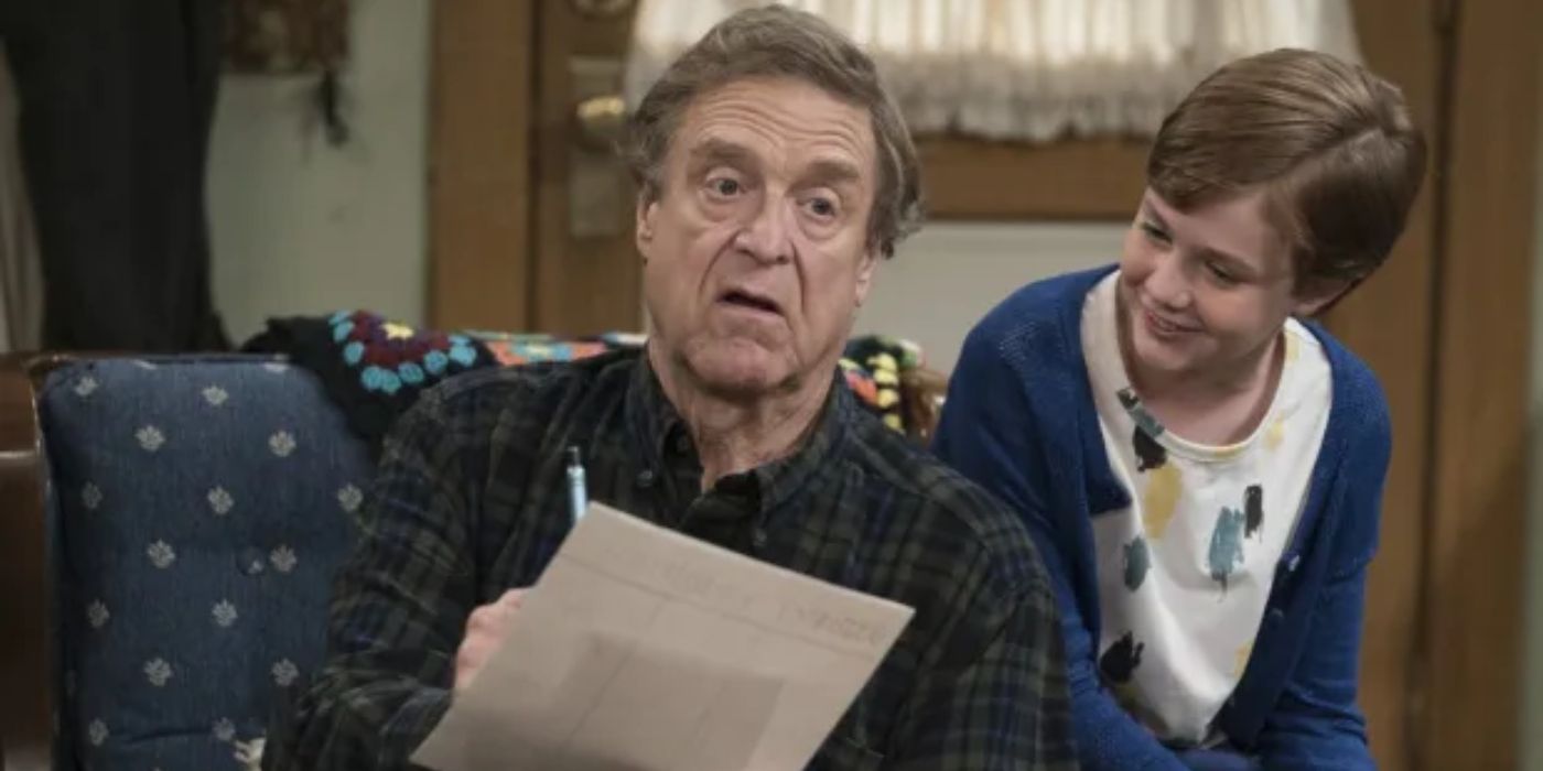 Dan (John Goodman) writing something and looking confused next to Mark (Ames McNamara) in The Conners